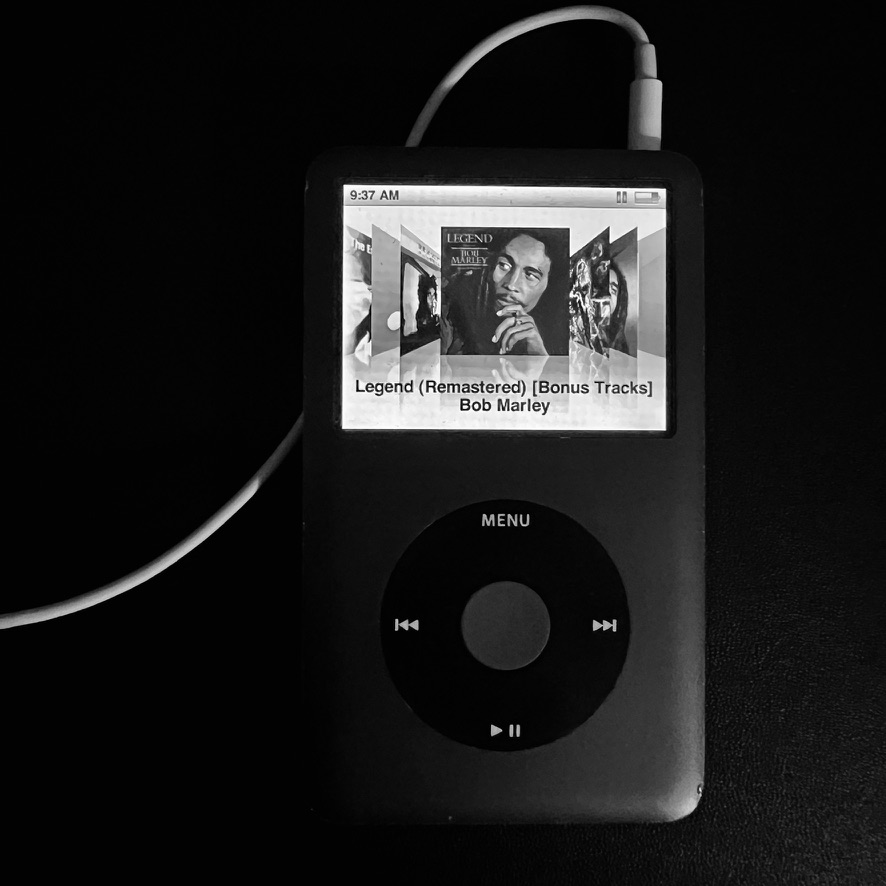 black and white photo of an iPod classic with headphones plugged in and a Bob Marley album showing on the screen